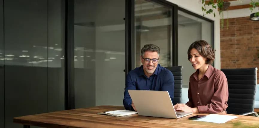 Two colleagues reviewing work on a laptop in a meeting room